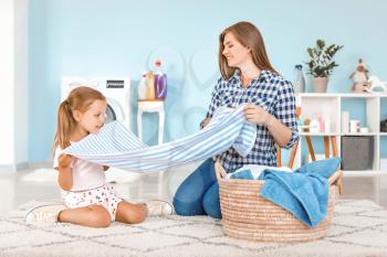 Woman and her little daughter doing laundry at home�