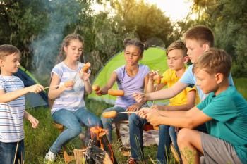 Group of children cooking sausages on campfire�