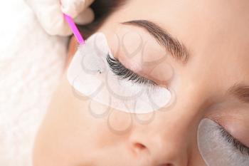 Young woman undergoing eyelash extension procedure in beauty salon, closeup�