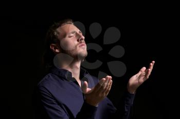Religious young man praying on dark background�