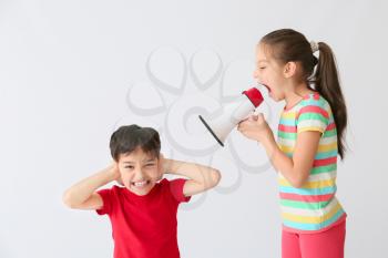 Little girl with megaphone screaming on boy against light background�