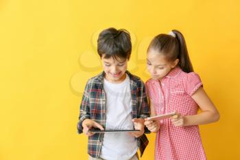 Cute little children with tablet computer and mobile phone on color background�