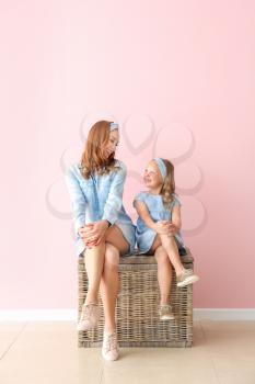 Beautiful woman and her little daughter sitting on wicker box near color wall�