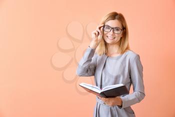 Beautiful female teacher with book on color background�