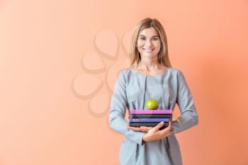 Beautiful female teacher with books and apple on color background�