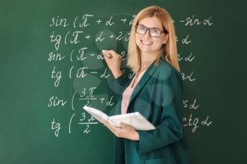 Beautiful math teacher with book near blackboard in classroom�