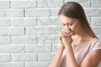 Religious young woman praying against brick wall�