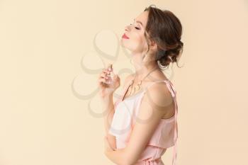 Beautiful young woman with bottle of perfume on light color background�