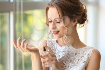 Beautiful young bride with bottle of perfume indoors�