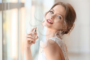 Beautiful young bride with bottle of perfume indoors�