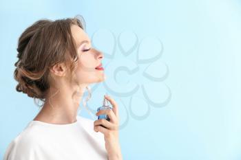 Beautiful young woman with bottle of perfume on color background�