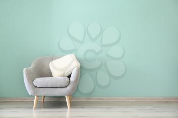 Comfortable armchair near color wall in room�