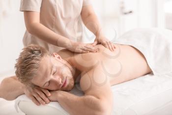 Handsome young man receiving massage in spa salon�