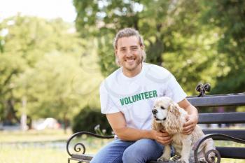 Male volunteer with cute dog sitting on bench outdoors�