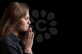 Religious young woman praying to God on dark background�