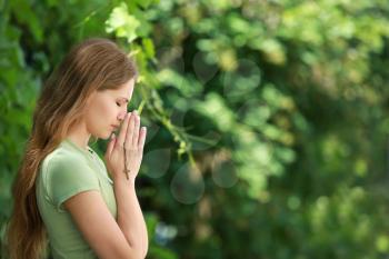 Religious woman praying to God outdoors�