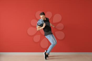 Handsome young man dancing against color wall�