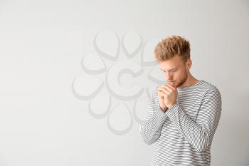 Religious young man praying to God on light background�