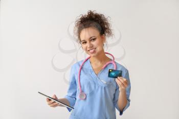 African-American doctor with credit card and tablet computer on light background�