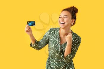 Happy African-American woman with credit card on color background�