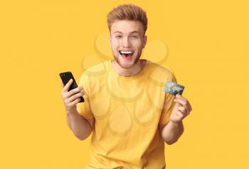 Happy young man with credit card and mobile phone on color background�