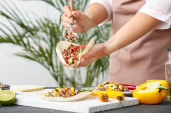 Woman preparing tasty fresh tacos in kitchen�