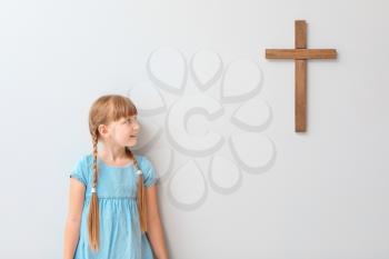 Little girl near light wall with cross�