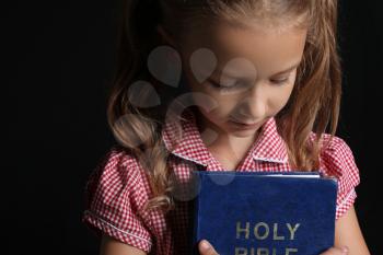 Cute little girl with Bible on dark background�