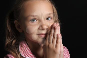 Praying little girl on dark background�