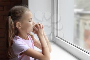 Praying little girl near window�