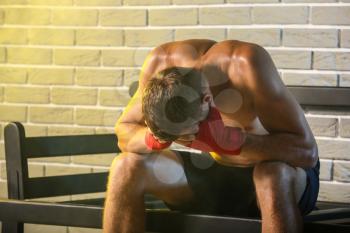 Upset male boxer sitting on bench against brick wall�