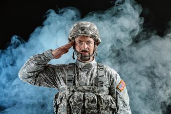 Saluting soldier on dark background with smoke�