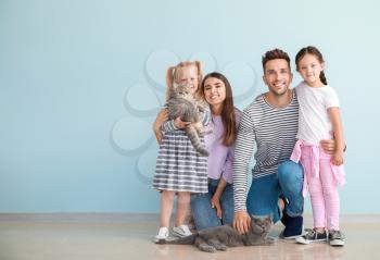 Happy family with cute cats near light wall�