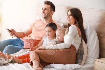 Happy family watching TV on bed at home�