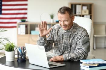 Mature male soldier using laptop in headquarters building for communication with his family�