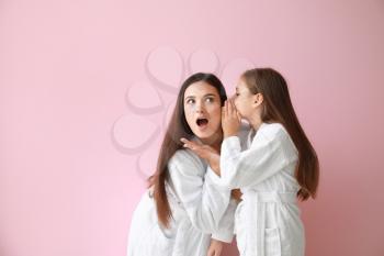 Little girl telling mother her secret on color background�
