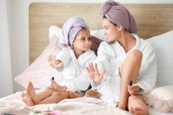 Mother and her little daughter in bathrobes manicuring nails in bedroom�