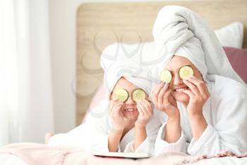 Mother and her little daughter in bathrobes and with cucumber slices in bedroom�