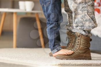 Child standing of feet of his military father at home�