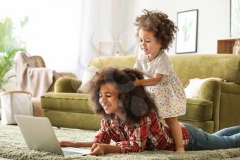 Cute African-American sisters with laptop watching cartoons at home�
