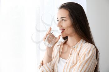 Morning of beautiful young woman drinking water near window�