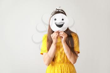 Woman hiding face behind sheet of paper with drawn emoticon on grey background�