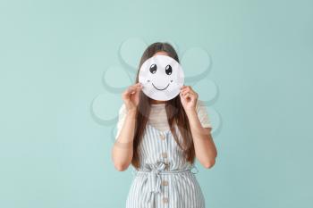Woman hiding face behind sheet of paper with drawn emoticon on color background�