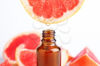 Citrus essential oil dripping from grapefruit into bottle on white background�