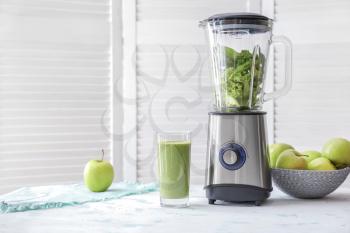 Glass of healthy smoothie and blender with ingredients on table�