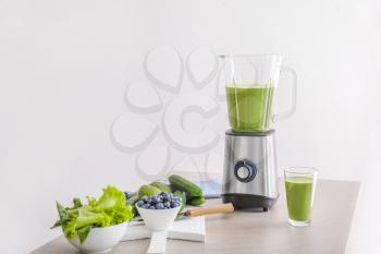 Glass of healthy smoothie, blender and ingredients on table�