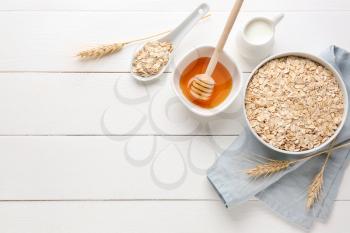 Bowl with raw oatmeal, honey and milk on white wooden table�