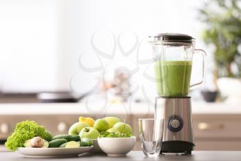 Blender with tasty smoothie and ingredients on table in kitchen�
