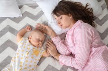 Mother and cute little baby sleeping on bed�
