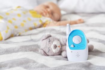 Modern baby monitor and toy on bed of sleeping infant�